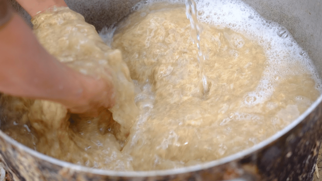 Une fois le giang ramolli, il est pilé puis filtré pour retirer les fibres grossières. La pâte obtenue est mélangée à de l’eau et remuée jusqu’à devenir homogène, laissant apparaître de fines fibres prêtes à former le papier.